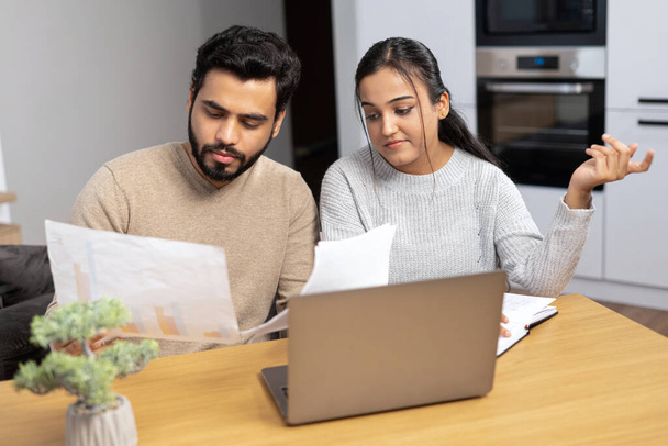 Serious young couple study documents together, have serious looks, dressed in casual wear, plan their budget, pose in spacious light room, do paperwork - Foto, imagen