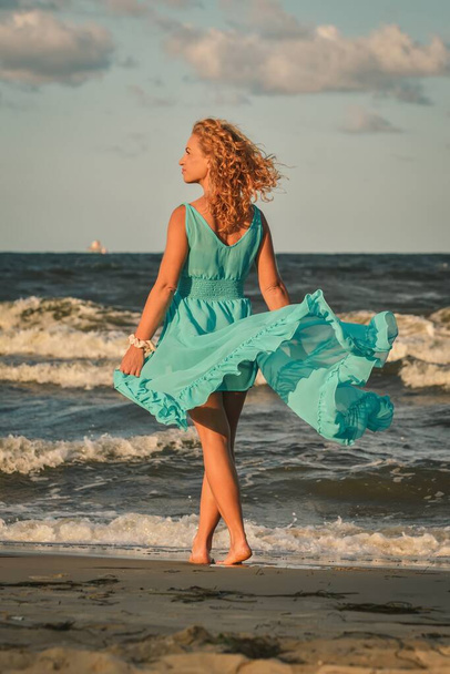 Beautiful blonde haired woman on the beach. Girl in a blue dress at the Polish seaside. - Фото, изображение