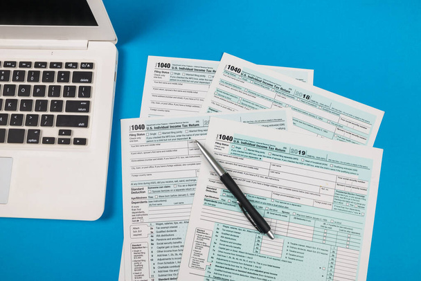 Vista superior de los formularios de impuestos 1040 con portátil y pluma sobre fondo azul aislado. - Foto, Imagen