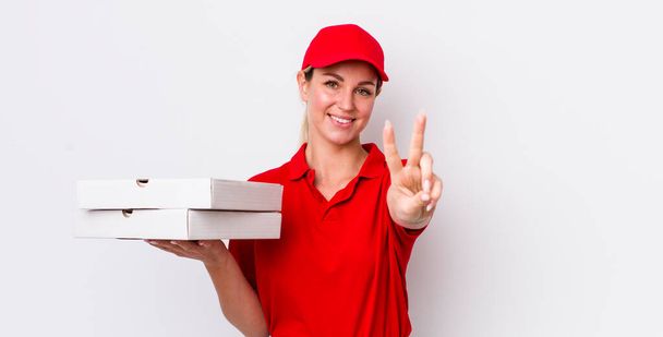 blonde pretty woman smiling and looking happy, gesturing victory or peace. pizza delivery concept - 写真・画像