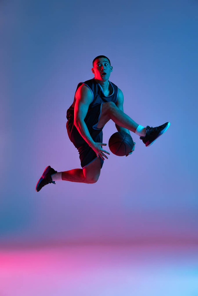 Young sportive man playing basketball isolated on blue studio background in neon light. Youth, hobby, motion, activity, sport concepts. - Zdjęcie, obraz