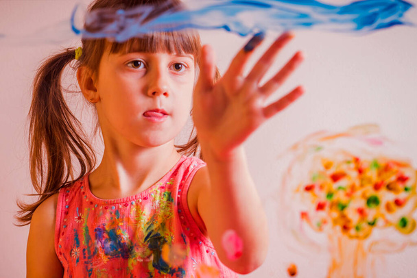 Искусство на стекле. Красивая маленькая девочка рисует на стекле. Счастливое детство, уроки живописи. Селективное фокусирование на глазах - Фото, изображение