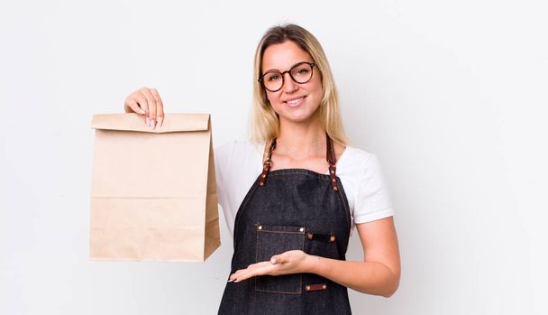 blonde pretty woman smiling cheerfully, feeling happy and showing a concept. delivery take away concept - Fotoğraf, Görsel