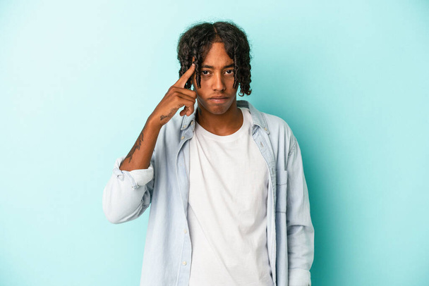 Молодой африканский американец, изолированный на синем фоне, указывая пальцем на висок, думая, сосредоточен на задаче. - Фото, изображение