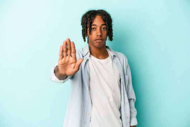 Junger afrikanisch-amerikanischer Mann isoliert auf blauem Hintergrund stehend mit ausgestreckter Hand, die Stoppzeichen zeigt und dich daran hindert. - Foto, Bild