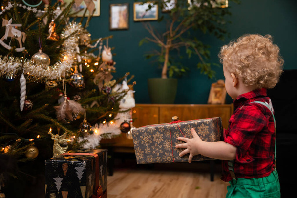 A two-year-old little boy carries a gift package on Christmas Day. - 写真・画像