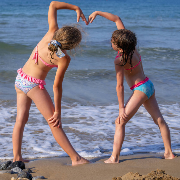 Pretty young girls making heart on the beach against sea background as symbol of summer holiday, rest and happiness. - Photo, Image