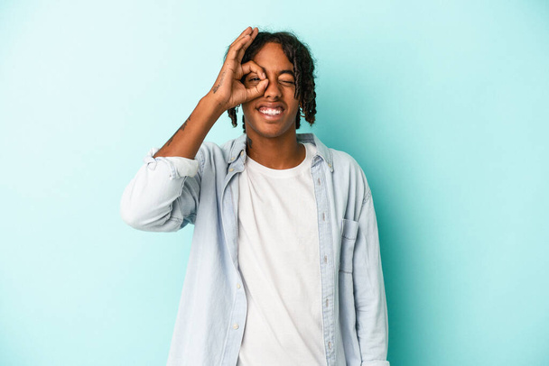 Young african american man isolated on blue background excited keeping ok gesture on eye. - Foto, Imagen