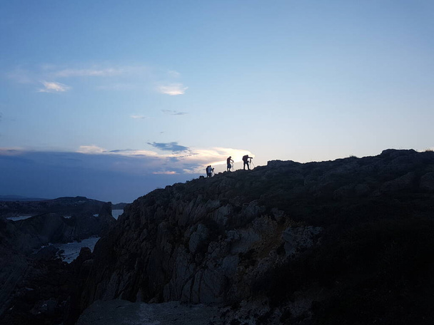 Mensen silhouetten in de top van de klif wachten op de zonsondergang. Blauwe lucht met wolken - Foto, afbeelding