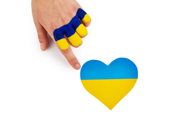 Женская рука с украинским флагом касается сердца Украины на изолированном белом фоне. Концепция прекращения войны, независимости Украины. Патриотизм и любовь к стране.  - Фото, изображение