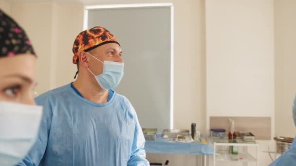 Trzech lekarzy w pracy działających w teatrze chirurgiczne zapisanie pacjenta i patrząc na życie monitora. Resuscytacji medycyna zespół noszenie maski ochronne zapisanie pacjenta. Chirurgia i koncepcji awaryjnego - Materiał filmowy, wideo
