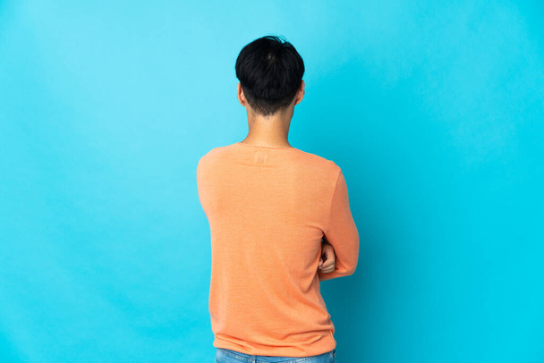 Νεαρός Κινέζος απομονωμένος σε μπλε φόντο στην πίσω θέση - Φωτογραφία, εικόνα