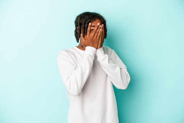 Jonge Afro-Amerikaanse man geïsoleerd op blauwe achtergrond knipperen door vingers bang en nerveus. - Foto, afbeelding