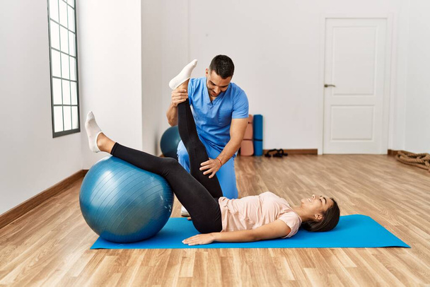 Latein Mann und Frau in Physiotherapeutenuniform bei einer Reha-Sitzung mit Fitnessball im Reha-Zentrum - Foto, Bild