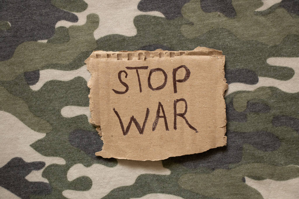 Alto a la guerra está escrito en papel que se encuentra en el uniforme militar de camuflaje del soldado, acción de protesta, ropa militar - Foto, imagen