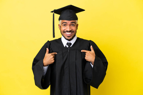 Mladý vysokoškolský absolvent kolumbijský muž izolované na žlutém pozadí s překvapivým výrazem obličeje - Fotografie, Obrázek