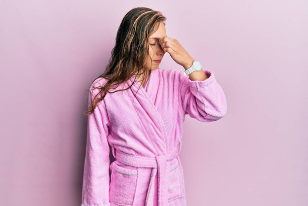 Young blonde woman wearing bathrobe tired rubbing nose and eyes feeling fatigue and headache. stress and frustration concept.  - Foto, afbeelding
