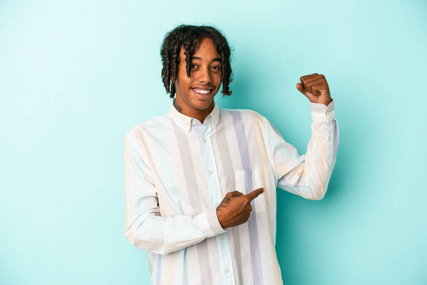 Young african american man isolated on blue background showing strength gesture with arms, symbol of feminine power - Foto, imagen