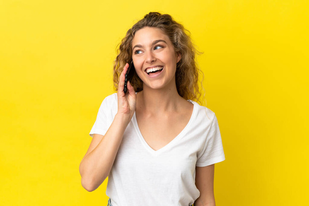 Young blonde woman using mobile phone isolated on yellow background looking side - Valokuva, kuva