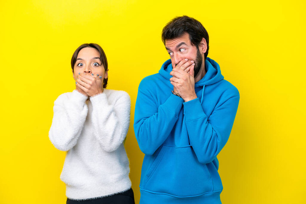 Young caucasian couple isolated on yellow background covering mouth with hands - Φωτογραφία, εικόνα