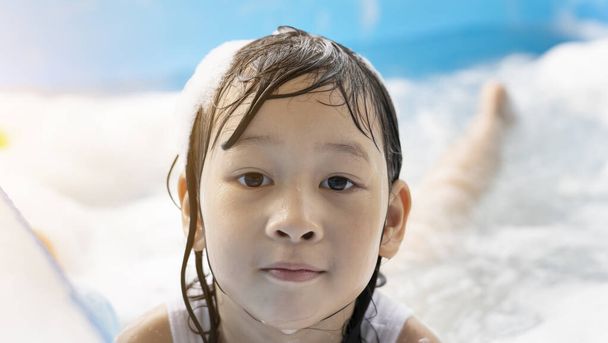 Cerca de la cara de la joven chica asiática feliz jugando en una piscina inflable. Jugar en el agua en casa durante las vacaciones de verano, la felicidad de los niños - Foto, Imagen