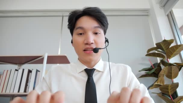 Mladý asijský muž sebevědomá podpora zástupce služby mluví s webovou kamerou. Asijský podnikatel ve sluchátkách komunikuje prostřednictvím konferenčního videohovoru. - Záběry, video
