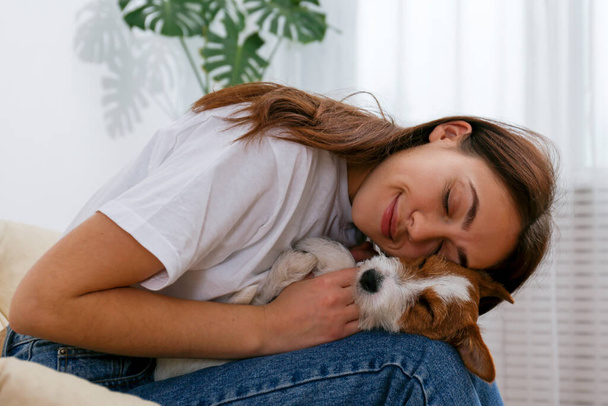 Portrait of young beautiful woman playing with her adorable four months old wire haired Jack Russel terrier puppy. Loving girl with rough coated pup having fun. Background, close up, copy space. - Foto, afbeelding