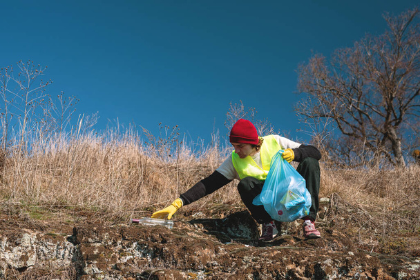 İnsan doğa eylemcisi elini mavi çöp torbasıyla boş cam şişeye uzatıyor. - Fotoğraf, Görsel