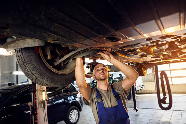 Auto monteur controleren loopwerk van auto op tankstation. Mannelijke werknemer oplossen probleem met de auto. Voertuigonderhoudsconcept - Foto, afbeelding