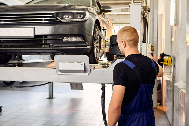 uto mechanic sets the car for diagnostics and configuration collapse-convergence . Car Wheels alignment equipment on stand in a repair station. - Photo, Image