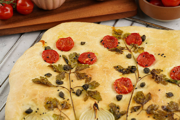 Floral painting focaccia, italian garden flatbread art with parsley, tomatoes, onions, sesame seeds and capers on light grey background - Valokuva, kuva