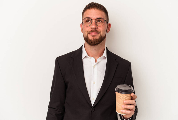 Young business caucasian man holding take away coffee isolated on white background dreaming of achieving goals and purposes - Foto, Imagem
