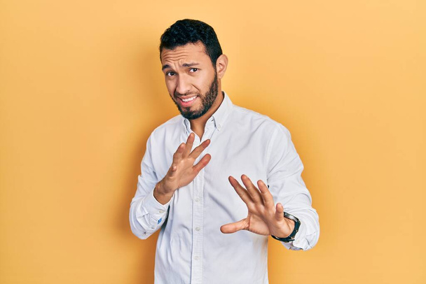 Hispanische Mann mit Bart trägt Business-Hemd angeekelten Ausdruck, ungehalten und ängstlich dabei Ekel Gesicht, weil Abneigung Reaktion. mit erhobenen Händen  - Foto, Bild
