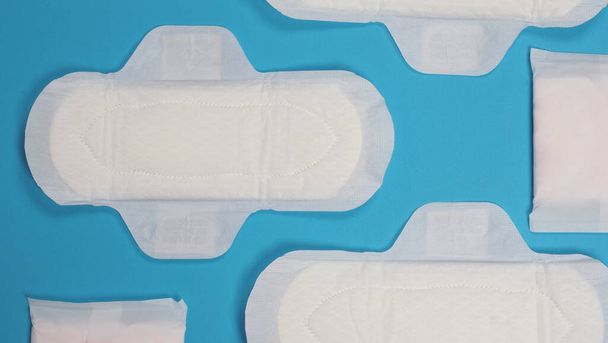 Dámské hygienické ubrousky na modrém pozadí. Horní pohled. Absorpční polštářky, které nosí ženy, aby absorbovaly menstruační krev. Pohodlné bílé hygienické ubrousky umístěné na světle modrém papíru. Reprezentativní koncept hygieny - Fotografie, Obrázek