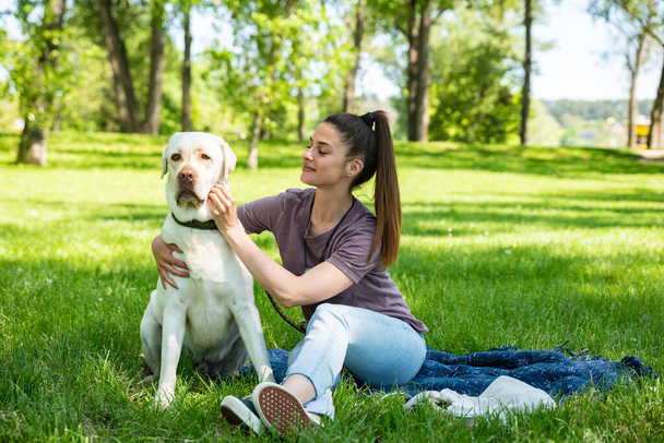 Young beautiful woman in the park with her pet dog white Labrador Retriever that she adopt from the pet shelter to give him good life and love. Female animal lover with her adopted puppy having fun. - Φωτογραφία, εικόνα