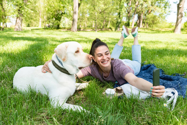 Jeune belle femme dans le parc avec son chien blanc Labrador Retriever qu'elle adopte du refuge pour animaux de compagnie pour lui donner une bonne vie et de l'amour. Femme amoureuse des animaux avec son chiot adopté s'amuser. - Photo, image
