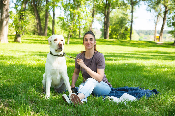 Young beautiful woman in the park with her pet dog white Labrador Retriever that she adopt from the pet shelter to give him good life and love. Female animal lover with her adopted puppy having fun. - Fotografie, Obrázek