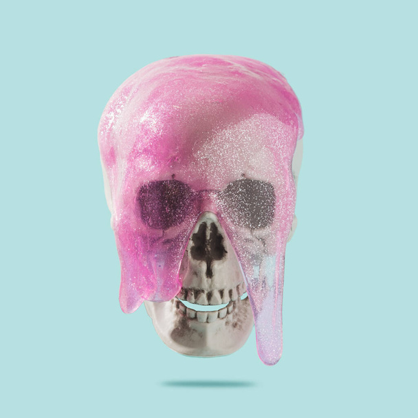 Crâne humain avec goo rose dégoulinant sur un fond bleu pastel. Cyber vie, concept Santa Muerte. - Photo, image