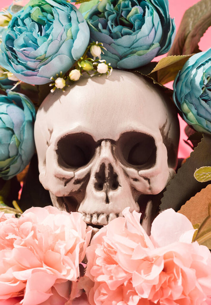 Череп человека окружен голубыми и розовыми цветами. День мертвых, Санта Муэрте концептуальный фон. - Фото, изображение