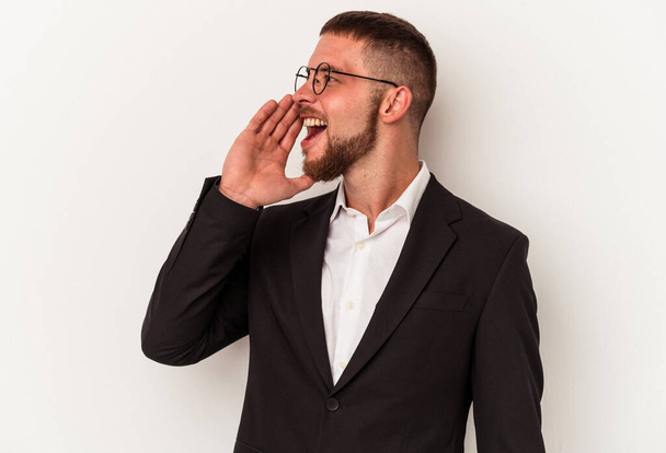 Молодой кавказский бизнесмен изолирован на белом фоне крича и держа ладонь у открытого рта. - Фото, изображение