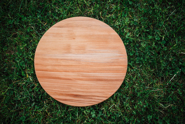 Round wooden cutting board for cutting on green grass - Photo, Image