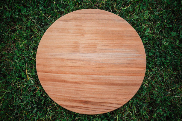 Кругла дерев'яна обробна дошка для різання на зеленій траві
 - Фото, зображення