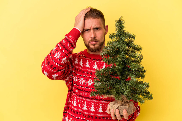 Nuori valkoihoinen mies ostaa vähän puuta jouluksi eristetty keltainen tausta on järkyttynyt, hän on muistanut tärkeä kokous. - Valokuva, kuva