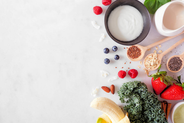 Healthy food side border. Smoothie making concept. Overhead view on a white marble background. Copy space. Fruit, yogurt, almond milk and a selection of ingredients. - Foto, Imagen