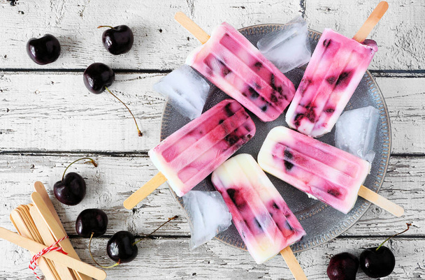 Plate of healthy cherry yogurt ice pops. Top down table scene over a rustic white wood background. - Foto, Imagem