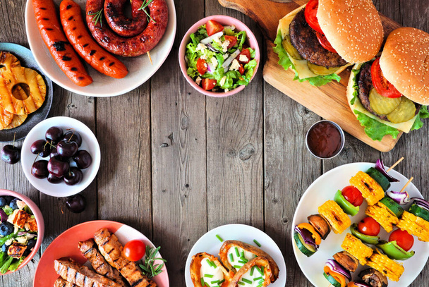 Summer BBQ or picnic food frame. Assorted burgers, grilled meat, vegetables, fruits, salad and potatoes. Above view on a dark wood background. Copy space. - Foto, Imagen