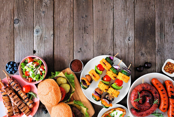 Summer BBQ or picnic food bottom border. Collection of burgers, grilled meat, vegetables, fruits, salad and potatoes. Top down view on a dark wood background. Copy space. - Photo, Image