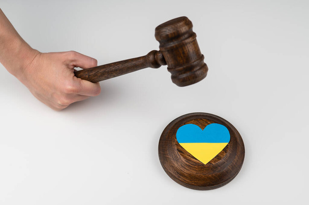 Woman hitting the judges gavel on the heart with the flag of Ukraine on a white background.  - 写真・画像