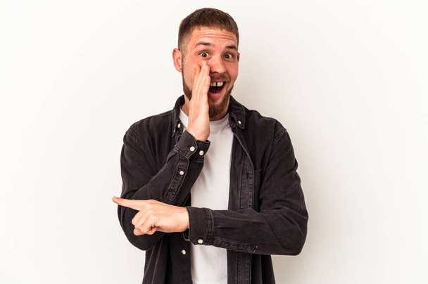 Young caucasian man with diastema isolated on white background saying a gossip, pointing to side reporting something. - 写真・画像