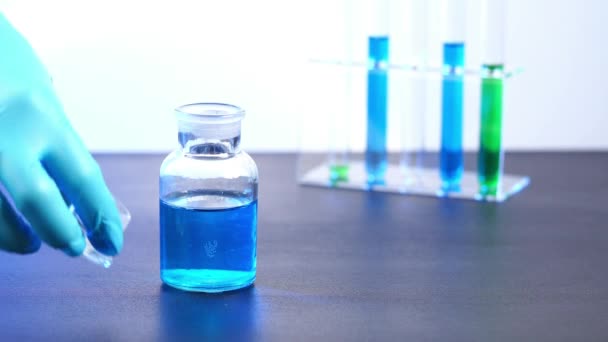 Ensayo químico La preparación verde en un matraz de vidrio se vierte en un recipiente de vidrio. - Imágenes, Vídeo